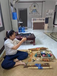 a woman sitting on the floor next to a table at Ban Loom Guesthouse & Weaving Workshop in Luang Prabang