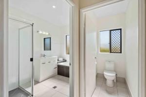 a white bathroom with a toilet and a sink at The Seahaven - Modern 5 Bedroom Family Home Close to Beach in Pialba +24 photos