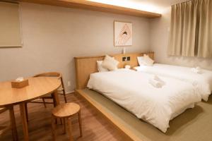 two beds in a small room with a table and a table and chairs at SOULEIADO Shinosaka in Osaka