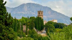 a church with a mountain in the background with trees at Casa Lia in Alcocer de Planes