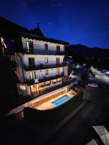 a large white building with a swimming pool next to a street at Chalet Fiocco Di Neve in Pinzolo