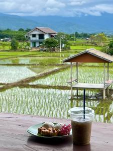 a plate of food and a drink on a table with a rice field at บ้านมาดีโฮมสเตย์ in Ban Huai La