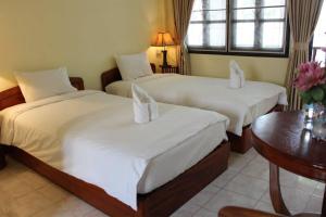 a bedroom with two beds with white sheets and a table at Dokban Hotel in Luang Prabang