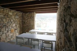 Habitación con mesas, sillas y pared de piedra. en The Camp Doniños, en Vila Da Area