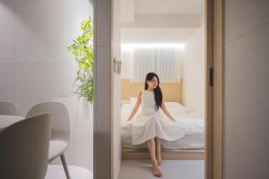 a woman in a white dress sitting on a bed at 더하다 in Busan