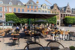 an outdoor cafe with tables and chairs and an umbrella at Bambu Kitchen & Bar - Hotel Restaurant in Haarlem