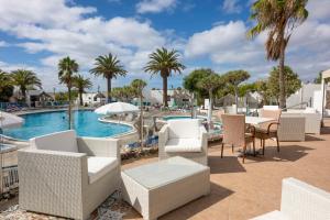 a patio with chairs and a pool with palm trees at Ona Las Casitas in Playa Blanca