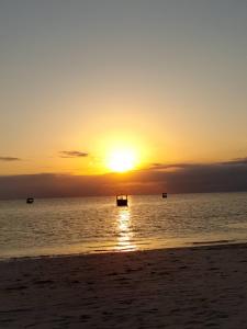 a sunset on the beach with a boat in the water at Kwetu nungwi in Kinyasini