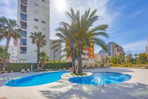 a swimming pool with palm trees and buildings at Apartamento Larimar - PlusHolidays in Ifach