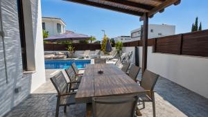 a patio with a wooden table and chairs next to a pool at Palm Tree Villa By Staycom in Oroklini