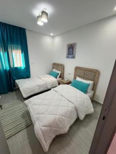 two beds in a room with blue curtains at Nador hola corniche in Nador