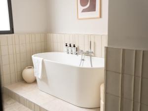 a white bath tub in a white tiled bathroom at Briqueterie Champagne, A Beauvallon Hotel & Spa in Vinay