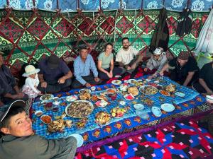 a group of people sitting around a table with food at Kamas Guesthouse in Kyzart