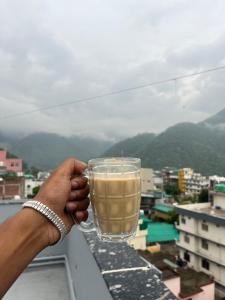 a person holding a glass of coffee on a balcony at Moonshiva stay and cafe in Rishīkesh