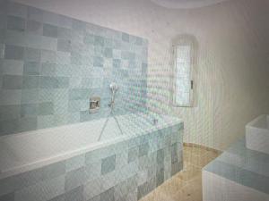 a bathroom with a tub with blue and gray tiles at Villa Sunset Bay in Baja Sardinia