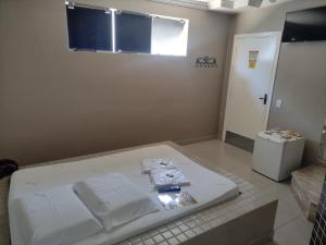 a room with a bed with white sheets and a refrigerator at Motel Classe A in Limeira