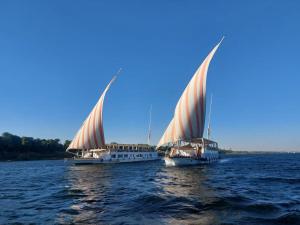 a boat with a large sail on the water at Three pyramids Dahabiya in Esna