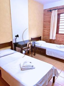 a room with two beds and a desk and a table at Pousada Siloé - Mosteiro de São Bento em Vinhedo in Vinhedo