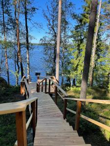 a wooden bridge over a lake with trees at Saimaanranta mökki in Kokkoniemi