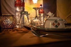 a table with a plate and glass bottles on it at Sahara Sunset Luxury Camp M'hamid in Mhamid