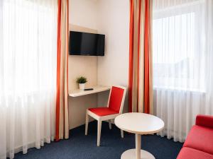 a room with a red chair and a table and a window at Hotel & Restaurant Möwchen in Norden