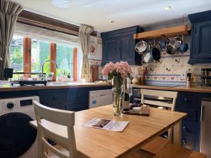 a kitchen with blue cabinets and a wooden table with flowers at Wind in the Willows Moreton in Marsh in Moreton in Marsh