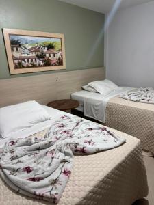 a hotel room with two beds and a blanket at Hotel Guerra - Pousada Montebelo in Jaguaruna