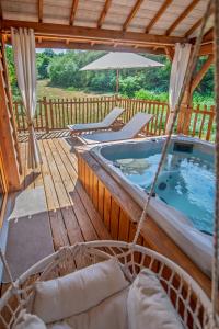 a hot tub on a deck with chairs and an umbrella at Cabane La Douce Parenthèse - Spa & Sauna in Brive-la-Gaillarde