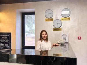 a woman standing at a counter with clocks on the wall at Avangard Hotel in Almaty