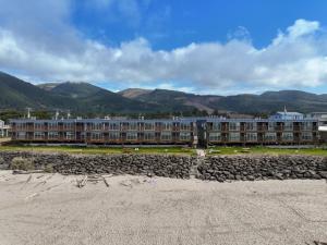 a building on a beach with mountains in the background at Surfside Resort in Rockaway Beach