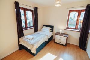 a bedroom with a bed and a nightstand and two windows at The Welsh Hideaway in Llanberis