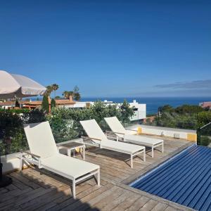 a group of white lounge chairs on a deck with the ocean at Casa Azul in Luz
