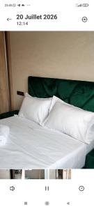 a bed with white sheets and a green head board at Résidence Hala in Tan-Tan