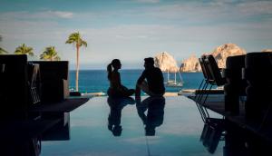 a couple sitting on the edge of a pool with the ocean at ME by Meliá Cabo - Adults Only in Cabo San Lucas