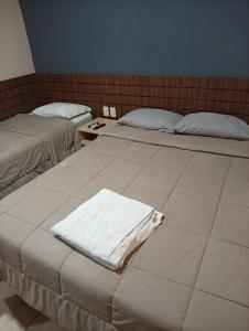 two beds in a hotel room with white sheets at Hotel Central Cardinal Pedro Juan Caballero in Pedro Juan Caballero