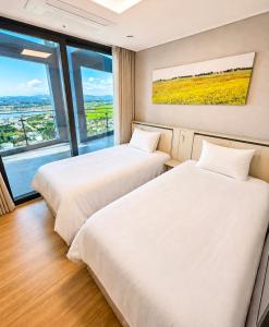 two beds in a room with a large window at 플럼바고올스위트34 in Chosan-ni