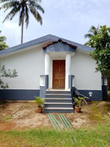 a white house with a wooden door and stairs at Cabo De Rama Cottage in Cola