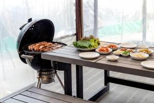 a table with a grill and plates of food at Samcheok The Ggeullim Pension in Samcheok