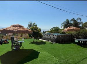 a lawn with tables and straw umbrellas and a pool at לרניקה - יחידות אירוח in Qiryat Shemona