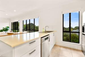 a kitchen with white cabinets and a sink and windows at Palm Cove Retreat I heated pool I Family home in Palm Cove