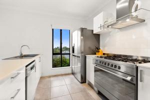 a white kitchen with a stove and a window at Palm Cove Retreat I heated pool I Family home in Palm Cove