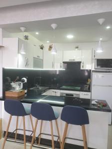 a kitchen with white cabinets and blue bar stools at Appart Cosy in Fnidek