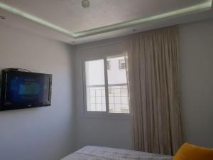 a bedroom with a tv on the wall and a window at Appart Cosy in Fnidek