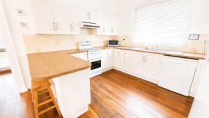 a white kitchen with white cabinets and a wooden floor at Teke Cottage in Wooli