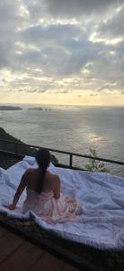 a woman sitting on a bed looking at the ocean at Suwehan Blue Ocean Cliff in Semarapura