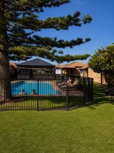 a pool with people sitting in chairs next to a tree at Geraldton's Ocean West Holiday Units & Short Stay Accommodation in Geraldton