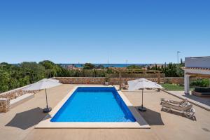 a swimming pool with two umbrellas on a patio at VILLA JESSELLA in Punta Prima