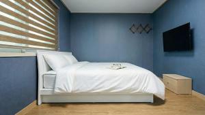 a bedroom with a white bed and a blue wall at Yeosu Trip Pension in Yeosu
