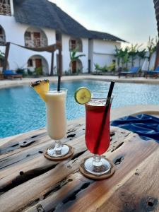 two cocktails on a wooden table next to a pool at Faro Resort in Nungwi