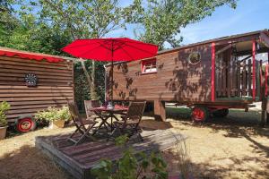 a table with a red umbrella next to a tiny house at Roulotte Champêtre Bella in Brix +12 photos